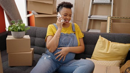 Foto de Mujer embarazada joven hablando en el teléfono inteligente sentado en el sofá en el nuevo hogar - Imagen libre de derechos