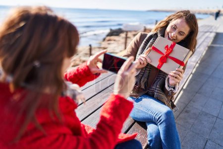 Téléchargez les photos : Deux femmes mère et fille font une photo par smartphone tenant cadeau au bord de la mer - en image libre de droit