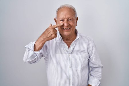 Téléchargez les photos : Homme âgé avec les cheveux gris debout sur fond isolé pointant avec le doigt de la main vers le visage et le nez, souriant gai. concept de beauté - en image libre de droit