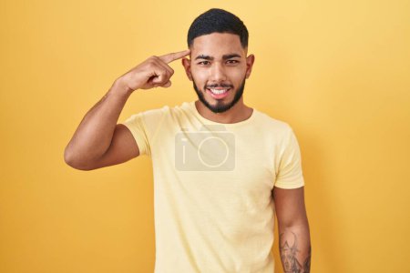 Téléchargez les photos : Jeune homme hispanique debout sur fond jaune souriant pointant vers la tête avec un doigt, bonne idée ou pensée, bonne mémoire - en image libre de droit