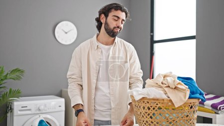 Photo for Young hispanic man looking basket with clothes with sad expression at street - Royalty Free Image