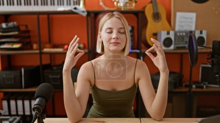 Téléchargez les photos : Jeune femme blonde musicienne assise sur la table faisant de l'exercice de yoga au studio de podcast - en image libre de droit
