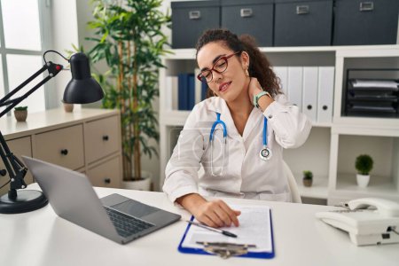 Photo for Young hispanic woman wearing doctor uniform and stethoscope suffering of neck ache injury, touching neck with hand, muscular pain - Royalty Free Image