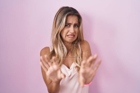 Téléchargez les photos : Young blonde woman standing over pink background disgusted expression, displeased and fearful doing disgust face because aversion reaction. - en image libre de droit