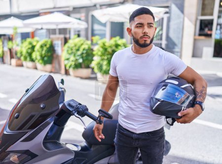 Photo for Young latin man holding helmet standing by motorbike at street - Royalty Free Image
