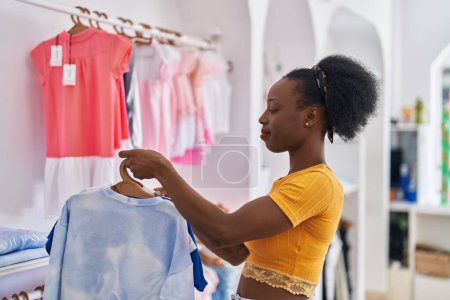 Photo for African american woman shop assistant hanging clothes on rack at clothing store - Royalty Free Image