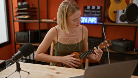 Téléchargez les photos : Jeune femme blonde musicienne ayant une leçon d'ukulélé en ligne au studio de musique - en image libre de droit