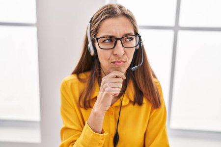 Photo for Young woman wearing call center agent headset serious face thinking about question with hand on chin, thoughtful about confusing idea - Royalty Free Image