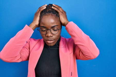 Téléchargez les photos : Belle femme noire debout sur fond bleu souffrant de maux de tête désespérés et stressés parce que la douleur et la migraine. mains sur la tête. - en image libre de droit