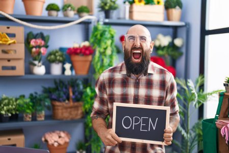 Photo for Young hispanic man with beard and tattoos working at florist holding open sign angry and mad screaming frustrated and furious, shouting with anger looking up. - Royalty Free Image