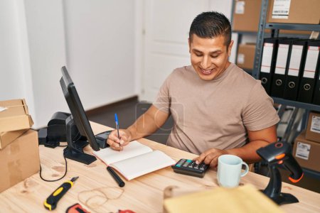 Téléchargez les photos : Jeune homme latin ecommerce travailleur d'affaires à l'aide d'une calculatrice écriture sur ordinateur portable au bureau - en image libre de droit