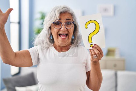 Photo for Middle age woman with grey hair holding question mark celebrating victory with happy smile and winner expression with raised hands - Royalty Free Image
