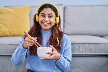 Photo for Young hispanic woman listening to music eating chinese food at home - Royalty Free Image