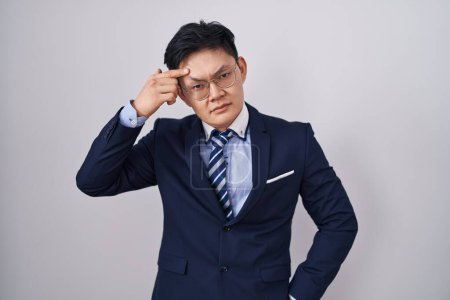 Photo for Young asian man wearing business suit and tie pointing unhappy to pimple on forehead, ugly infection of blackhead. acne and skin problem - Royalty Free Image