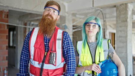 Téléchargez les photos : Hommes et femmes bâtisseurs debout avec une expression détendue tenant un casque de sécurité sur le chantier de construction - en image libre de droit