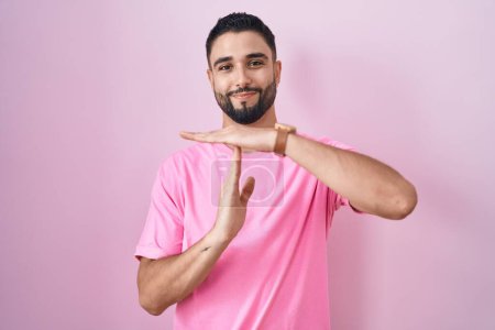 Photo for Hispanic young man standing over pink background doing time out gesture with hands, frustrated and serious face - Royalty Free Image