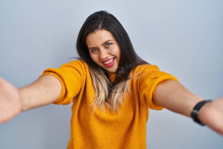 Photo for Young hispanic woman standing over isolated background looking at the camera smiling with open arms for hug. cheerful expression embracing happiness. - Royalty Free Image