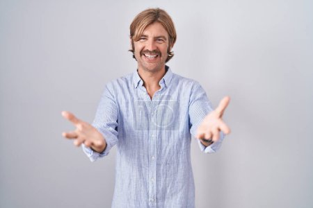 Photo for Caucasian man with mustache standing over white background smiling cheerful offering hands giving assistance and acceptance. - Royalty Free Image