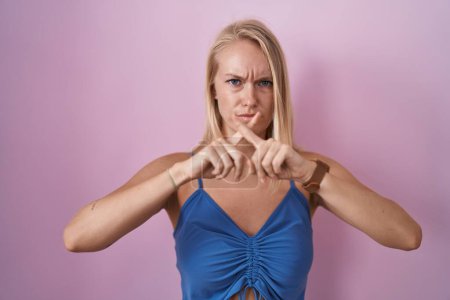 Téléchargez les photos : Jeune femme caucasienne debout sur fond rose expression de rejet croisant les doigts faisant signe négatif - en image libre de droit