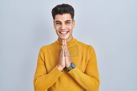 Photo for Young hispanic man standing over blue background praying with hands together asking for forgiveness smiling confident. - Royalty Free Image