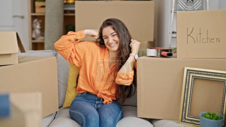 Photo for Young beautiful hispanic woman smiling confident sitting on sofa with winner expression at new home - Royalty Free Image