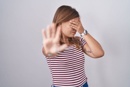 Téléchargez les photos : Jeune femme hispanique debout sur fond isolé couvrant les yeux avec les mains et faisant arrêter geste avec expression triste et peur. concept embarrassé et négatif. - en image libre de droit