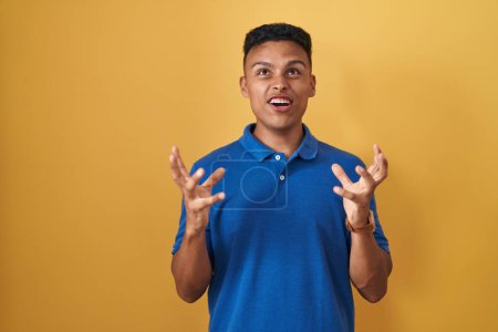 Téléchargez les photos : Young hispanic man standing over yellow background crazy and mad shouting and yelling with aggressive expression and arms raised. frustration concept. - en image libre de droit