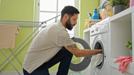 Photo for Young hispanic man washing clothes at laundry room - Royalty Free Image