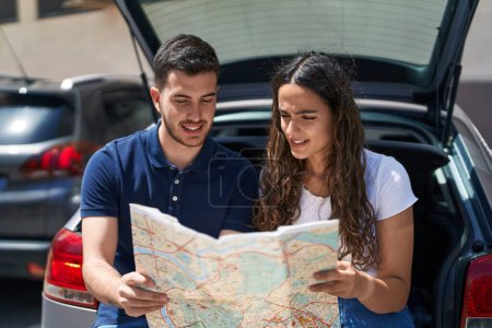 Photo for Young hispanic couple sitting on car trunk looking city map at street - Royalty Free Image