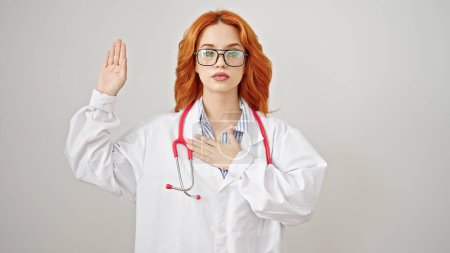 Téléchargez les photos : Jeune rousse femme médecin faire un serment avec la main sur la poitrine sur fond blanc isolé - en image libre de droit