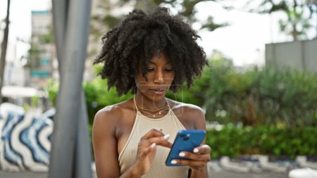 Photo for African american woman using smartphone with serious expression at park - Royalty Free Image
