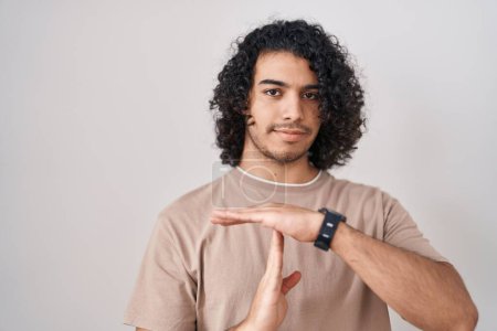 Téléchargez les photos : Homme hispanique avec les cheveux bouclés debout sur fond blanc faire un geste de temps avec les mains, visage frustré et sérieux - en image libre de droit