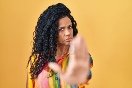 Photo for Middle age hispanic woman standing over yellow background doing stop sing with palm of the hand. warning expression with negative and serious gesture on the face. - Royalty Free Image