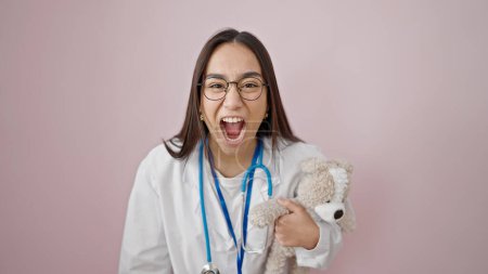 Photo for Young beautiful hispanic woman doctor angry and stressed holding teddy bear over isolated pink background - Royalty Free Image