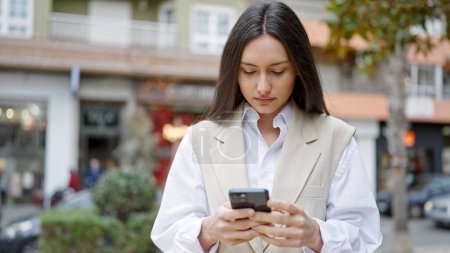 Photo for Young beautiful hispanic woman using smartphone with serious expression at street - Royalty Free Image