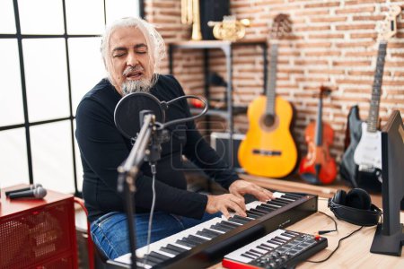 Photo for Middle age grey-haired man musician singing song playing piano at music studio - Royalty Free Image