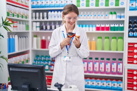 Foto de Joven mujer rubia farmacéutico escaneo pastillas botella en la farmacia - Imagen libre de derechos
