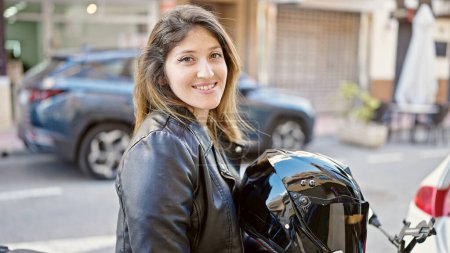 Foto de Joven mujer rubia sonriendo confiada sentada en motocicleta en la calle - Imagen libre de derechos