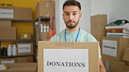 Téléchargez les photos : Jeune homme arabe bénévole détenant un paquet de dons au centre de bienfaisance - en image libre de droit