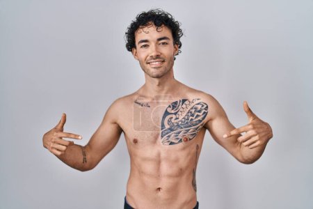 Foto de Hombre hispano de pie sin camisa mirando confiado con sonrisa en la cara, señalándose con los dedos orgullosos y felices. - Imagen libre de derechos