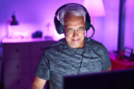 Téléchargez les photos : Moyen âge homme aux cheveux gris streamer jouer à un jeu vidéo en utilisant l'ordinateur à la salle de jeux - en image libre de droit