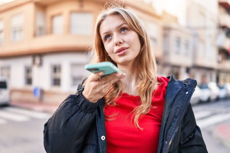 Téléchargez les photos : Jeune femme blonde souriant confiant parler sur le smartphone à la rue - en image libre de droit