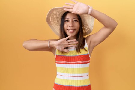 Téléchargez les photos : Femme chinoise du Moyen Age portant chapeau d'été sur fond jaune souriant joyeux jeu coup d'oeil un boo avec les mains montrant le visage. surpris et sortis - en image libre de droit