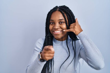 Photo for African american woman standing over blue background smiling doing talking on the telephone gesture and pointing to you. call me. - Royalty Free Image