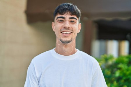 Téléchargez les photos : Jeune homme hispanique souriant confiant debout dans la rue - en image libre de droit