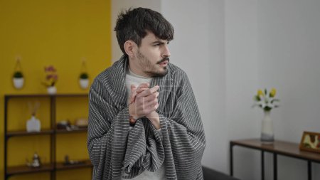 Photo for Young hispanic man feeling cold covered with blanket at home - Royalty Free Image