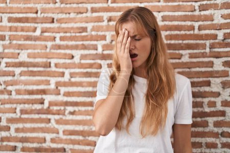 Photo for Young caucasian woman standing over bricks wall yawning tired covering half face, eye and mouth with hand. face hurts in pain. - Royalty Free Image