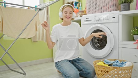 Foto de Mujer rubia joven escuchando música y bailando en la lavandería - Imagen libre de derechos