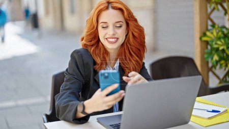 Photo for Young redhead woman business worker using laptop and smartphone at coffee shop terrace - Royalty Free Image