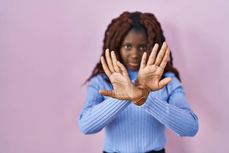 Foto de Mujer africana de pie sobre el fondo rosa expresión rechazo cruzando brazos y palmas haciendo signo negativo, cara enojada - Imagen libre de derechos